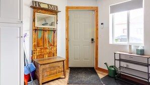A hallway with a wooden cabinet, a door, a window, and a small desk.