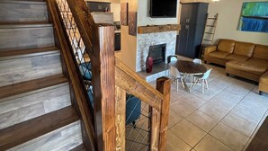 Uma escada de madeira com corrimão de metal leva a uma sala de estar com lareira, televisão na parede e um sofá.