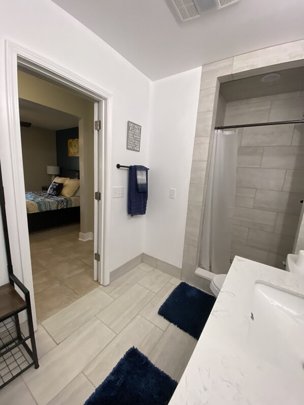 Ein modernes Badezimmer mit einem weißen Waschtisch, einer Dusche und einer sichtbaren Tür zu einem Schlafzimmer.