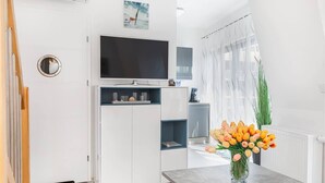 A modern kitchen with a TV, white cabinetry, and a vase of tulips on the counter.