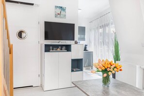 Uma cozinha moderna com televisão, armários brancos e um vaso de tulipas na bancada.