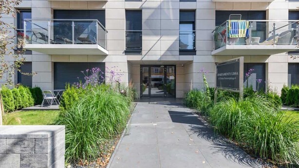 A modern building with a central entrance, two balconies, and a sign indicating 'APARTMENT LISS'.
