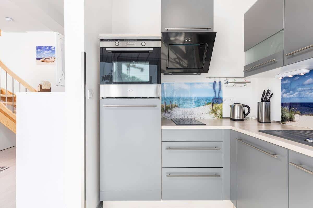 Una cocina moderna con electrodomésticos de acero inoxidable, un salpicadero con una escena de playa y una escalera que sube a un nivel superior.