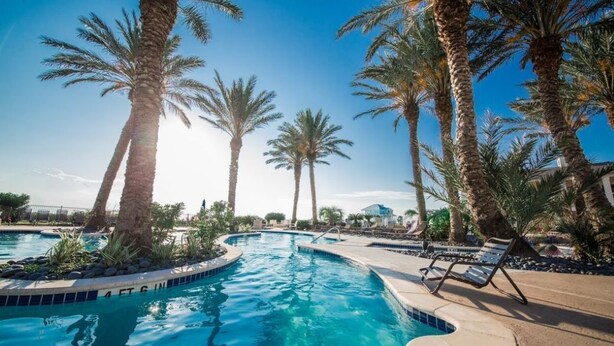 Una piscina con palmeras, sillas de descanso y un cielo azul despejado.