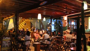 An outdoor café with wooden tables and chairs, a signboard for coffee, and a brick wall in the background. - Pousada dos Meros (Angra dos Reis)