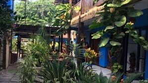 A courtyard with potted plants, a stone pathway, and a building with a thatched roof and blue walls. - Pousada dos Meros (Angra dos Reis)