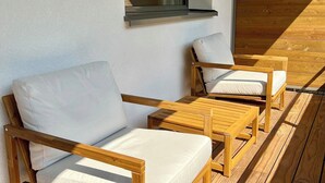 Een houten terras met twee houten stoelen en een kleine tafel, een raam met uitzicht op de lucht, en een houten vloer.