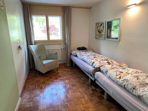 A small room with a wooden parquet floor, a single bed with floral bedding, a chair, a radiator, and a window with curtains. - Alte Gasse 9 Appartement/Fewo 4-Bettwohnung by Interhome (Engelberg)