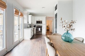 A modern kitchen with white cabinets, a microwave, and a stove. There is a dining table with chairs and a vase of flowers. - Sleek and Stylish Abode in Vibrant Neighborhood (New Orleans)