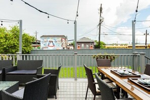 An outdoor patio with wicker furniture and a wooden table set for dining. - Sleek and Stylish Abode in Vibrant Neighborhood (New Orleans)