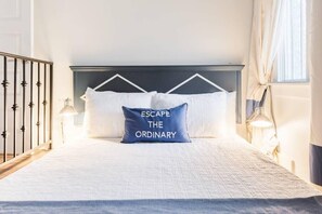 A neatly made bed with a pillow that reads "ESCAPE THE ORDINARY" in a hotel room with a simple, clean design. - Sleek and Stylish Abode in Vibrant Neighborhood (New Orleans)