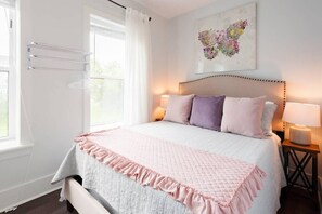 A bedroom with a bed, bedside lamps, a window with curtains, and a wall-mounted towel rack. - Sleek and Stylish Abode in Vibrant Neighborhood (New Orleans)