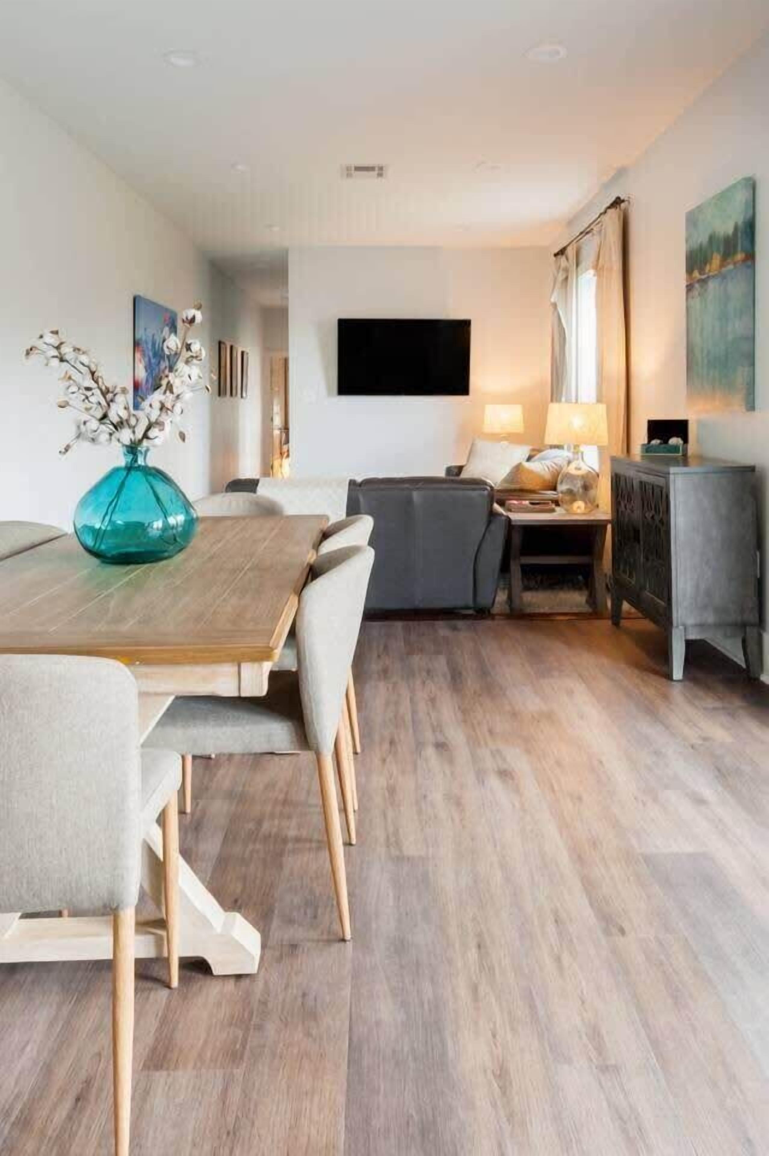 Un salon moderne comprenant un coin repas, un téléviseur à écran plat fixé au mur et un ensemble de canapés.