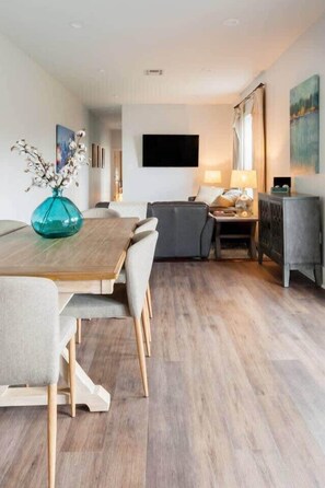 A modern living room with a wooden dining table, grey sofa, and a TV mounted on the wall. - Sleek and Stylish Abode in Vibrant Neighborhood (New Orleans)