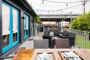 An outdoor patio with wooden tables and chairs, a covered seating area, and a view of a restaurant in the background. - Sleek and Stylish Abode in Vibrant Neighborhood (New Orleans)