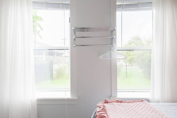 A bedroom with a bed, a window with curtains, and a metal rack on the wall. - Sleek and Stylish Abode in Vibrant Neighborhood (New Orleans)