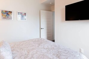 A bedroom with a bed, a television mounted on the wall, and two framed artworks on the wall. - Sleek and Stylish Abode in Vibrant Neighborhood (New Orleans)