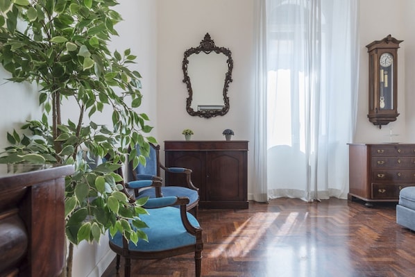 A room with a wooden floor, a blue upholstered chair, a wooden cabinet, a mirror, and a clock on the wall.