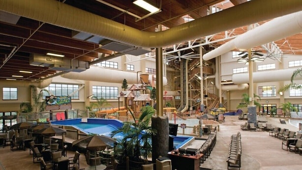 A spacious indoor area with a large pool, multiple seating areas, and a water slide.