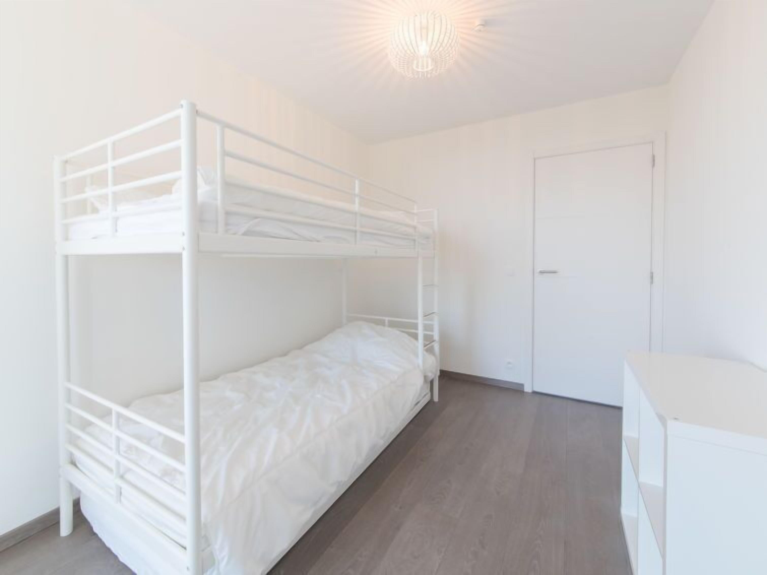 Une chambre avec un lit superposé, une porte blanche et une petite commode blanche.