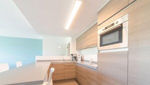 Una cocina moderna con armarios de madera, un microondas integrado y una gran mesa de comedor con sillas blancas.