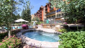 A hot tub surrounded by stone steps, with a pool table and umbrellas in the background. - Ski in, Ski out 3 Bedroom Mountain Residence in the Heart of Lionshead Village with Heated Slope Side Pool and Hot Tub (Vail)