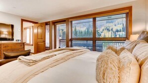 A bedroom with a large bed, wooden headboard, and a view of trees through the windows. - Ski in, Ski out 3 Bedroom Mountain Residence in the Heart of Lionshead Village with Heated Slope Side Pool and Hot Tub (Vail)