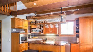 A modern kitchen with wooden cabinets, a granite countertop, a built-in oven, a sink, and a bar area with stools. - Tahkon rummikub by Interhome (Nilsiä)