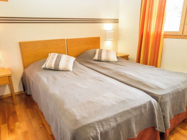 Una cama doble con cabecera de madera, dos almohadas, una mesita de noche y una ventana con cortinas.