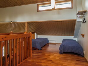 Una habitación con dos camas, piso de madera, techo inclinado y una ventana.
