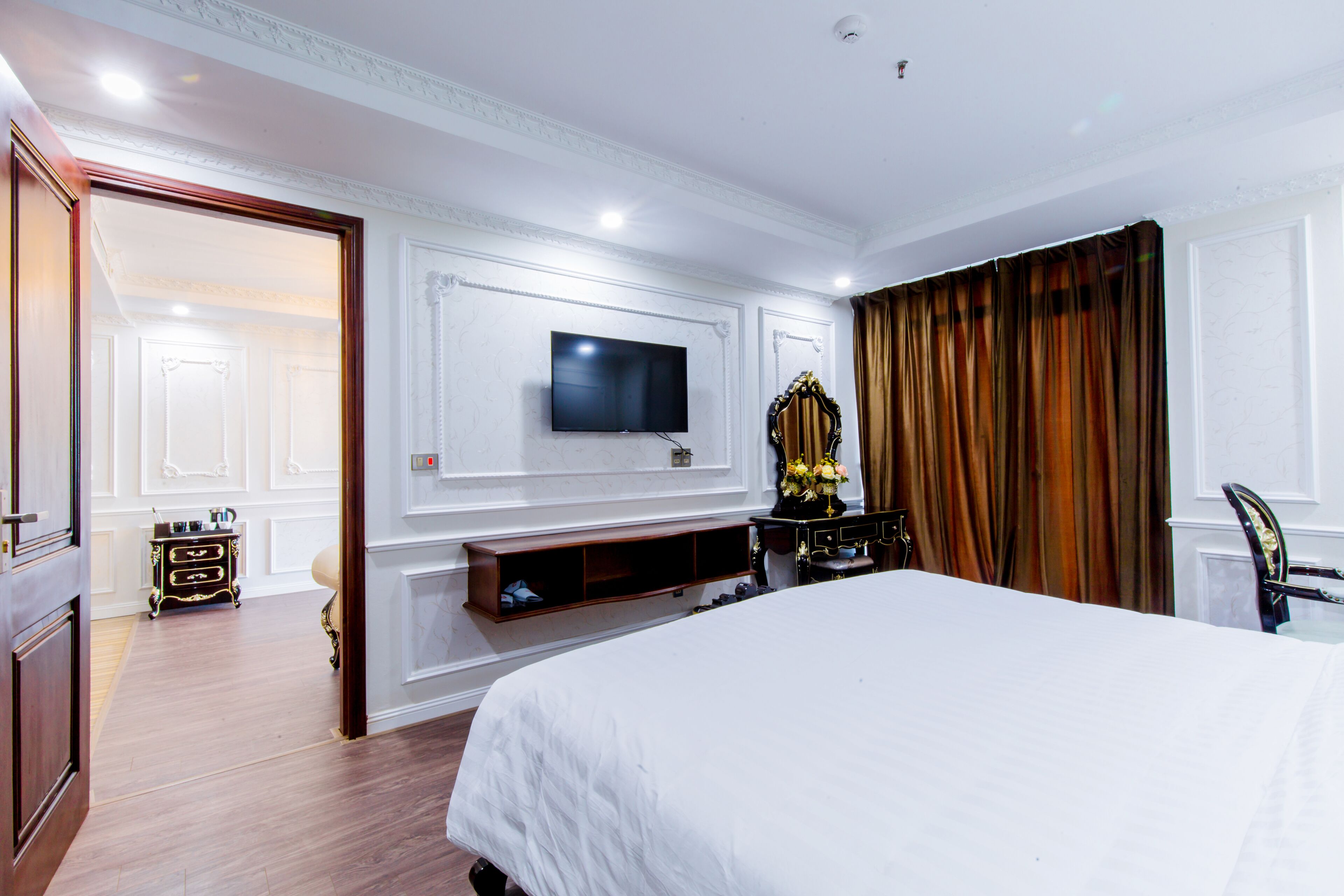 Una habitación de hotel con una cama grande, un televisor de pantalla plana montado en la pared, un tocador con espejo y un aparador de madera.