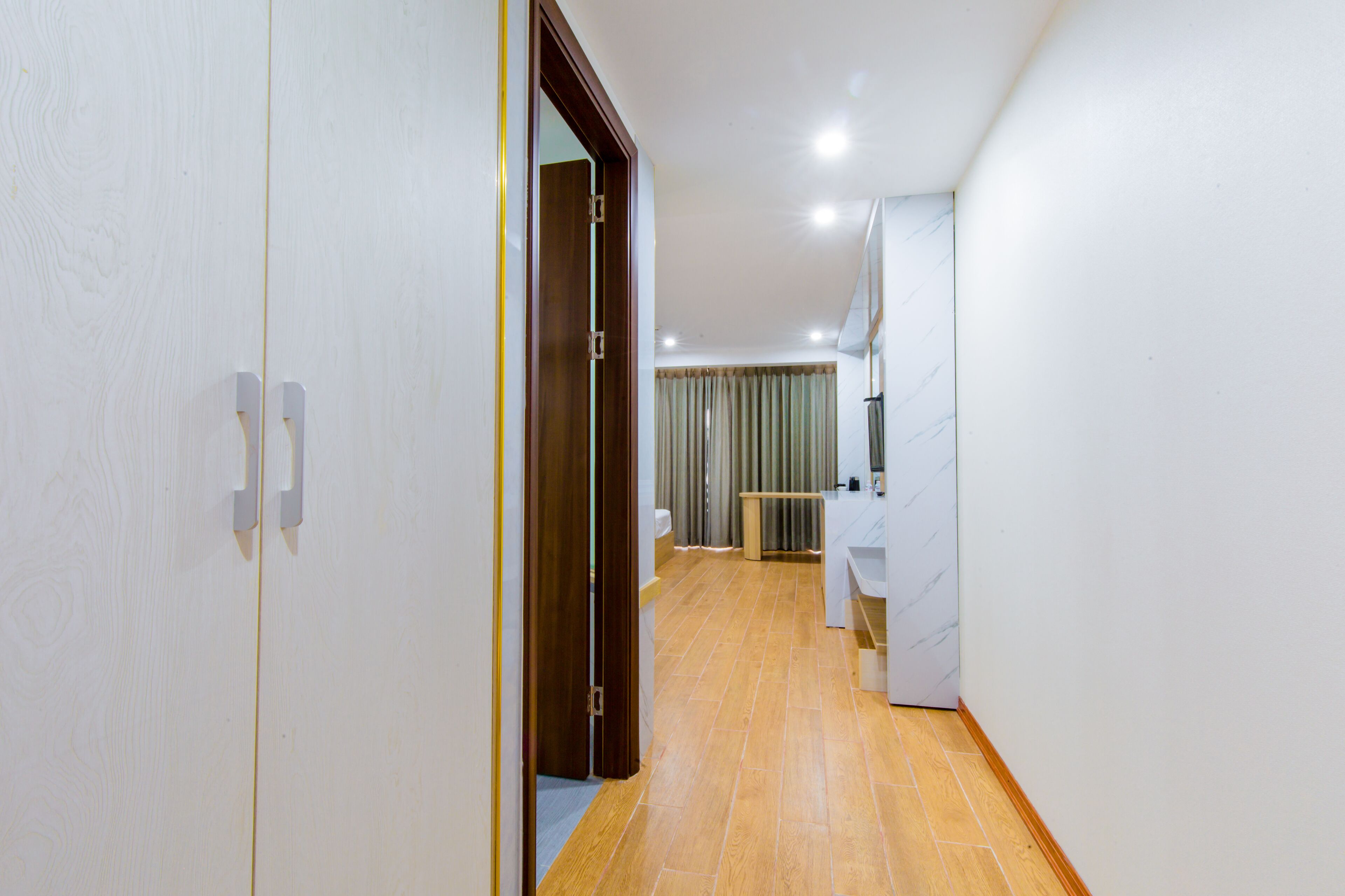 Un pasillo con piso de madera, una puerta y un baño con lavamanos y espejo blancos.