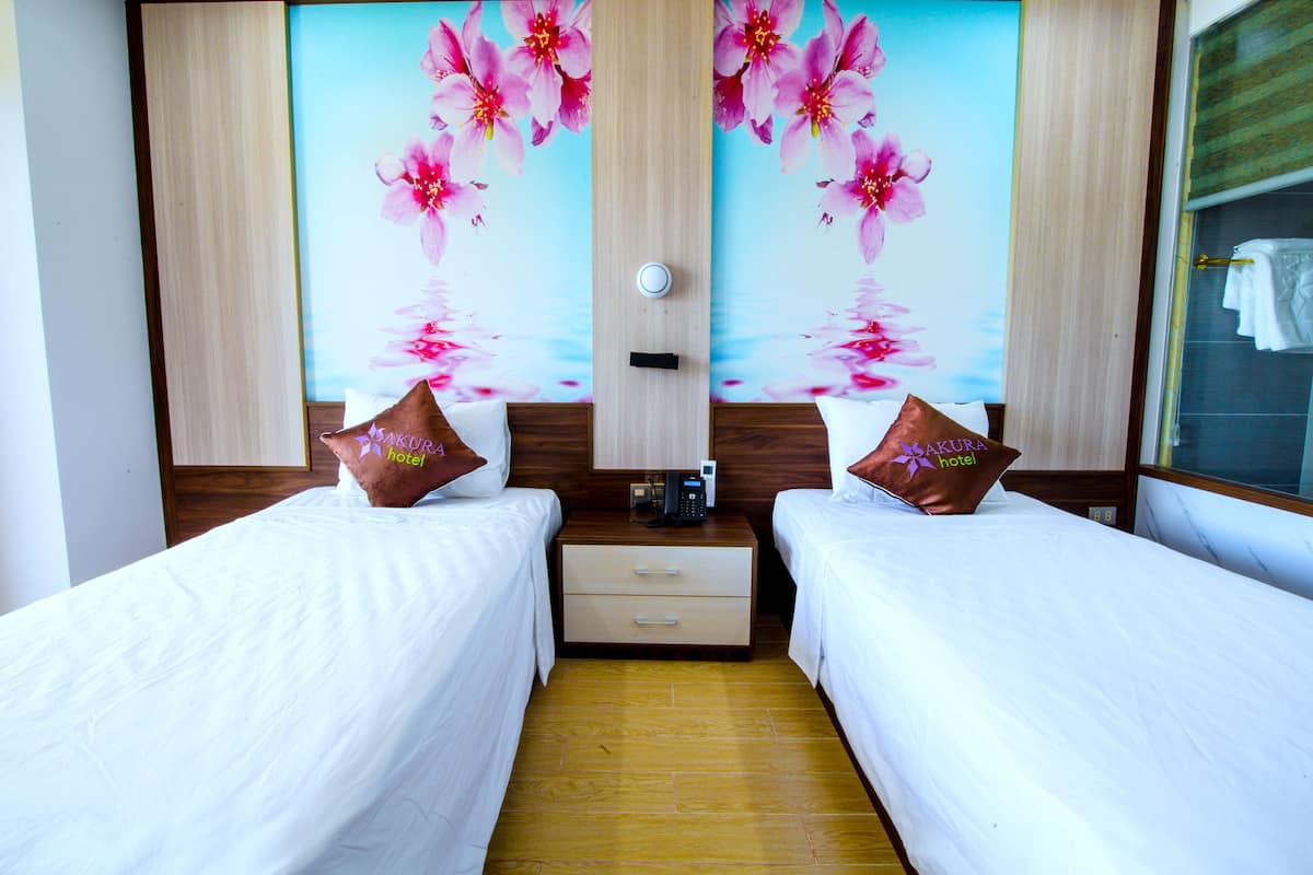 A hotel room with two single beds, a wooden floor, a large floral wall mural, and a small bedside table with a phone.