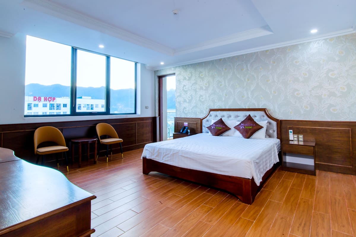 A hotel room with a large bed, two chairs, a desk, and a view of mountains through large windows.