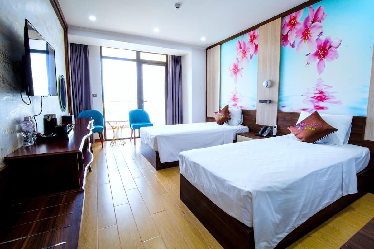 A hotel room with two beds, a desk, a chair, a TV, and a large window.