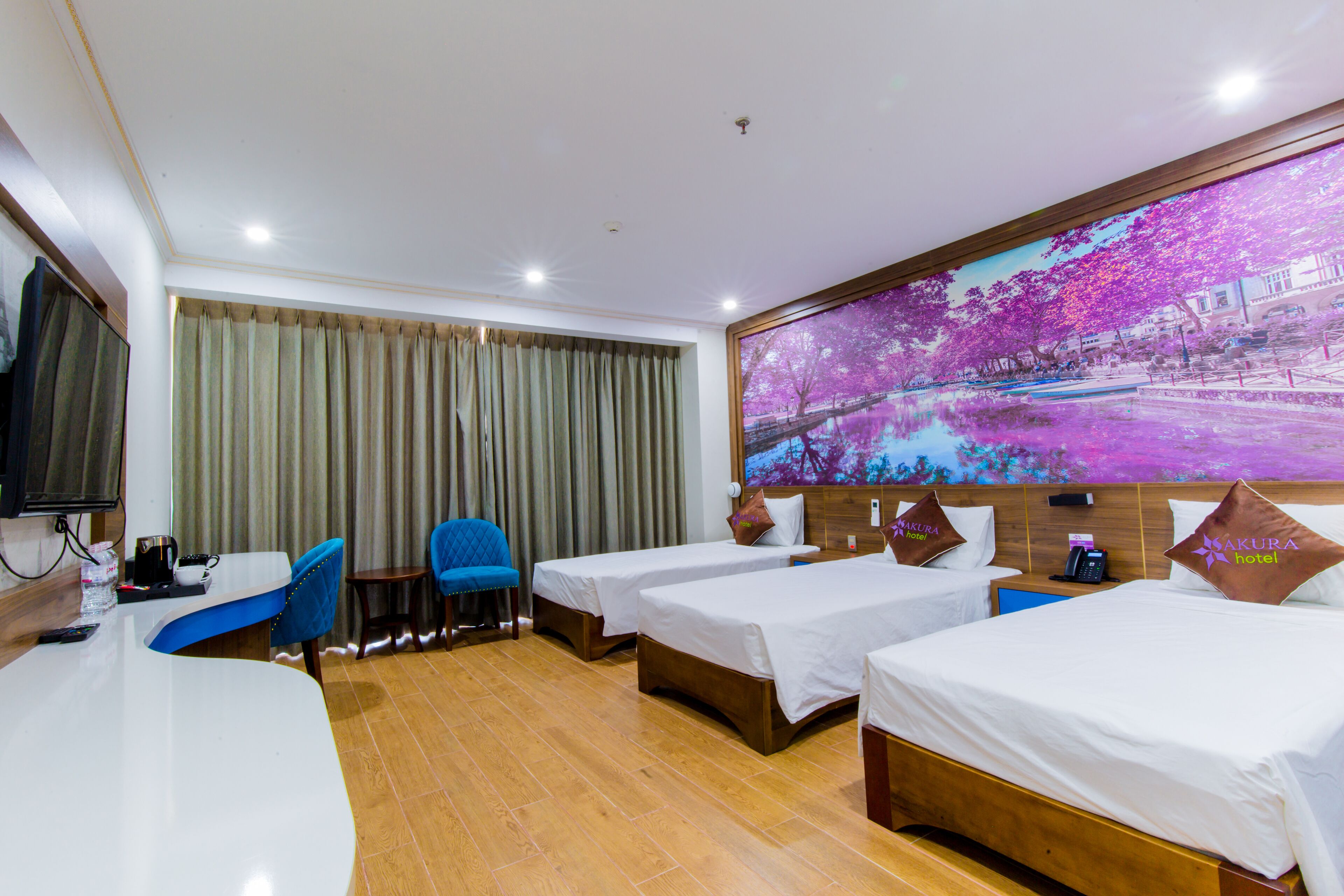 A hotel room with two single beds, a desk, a chair, a TV, and a large window with curtains.