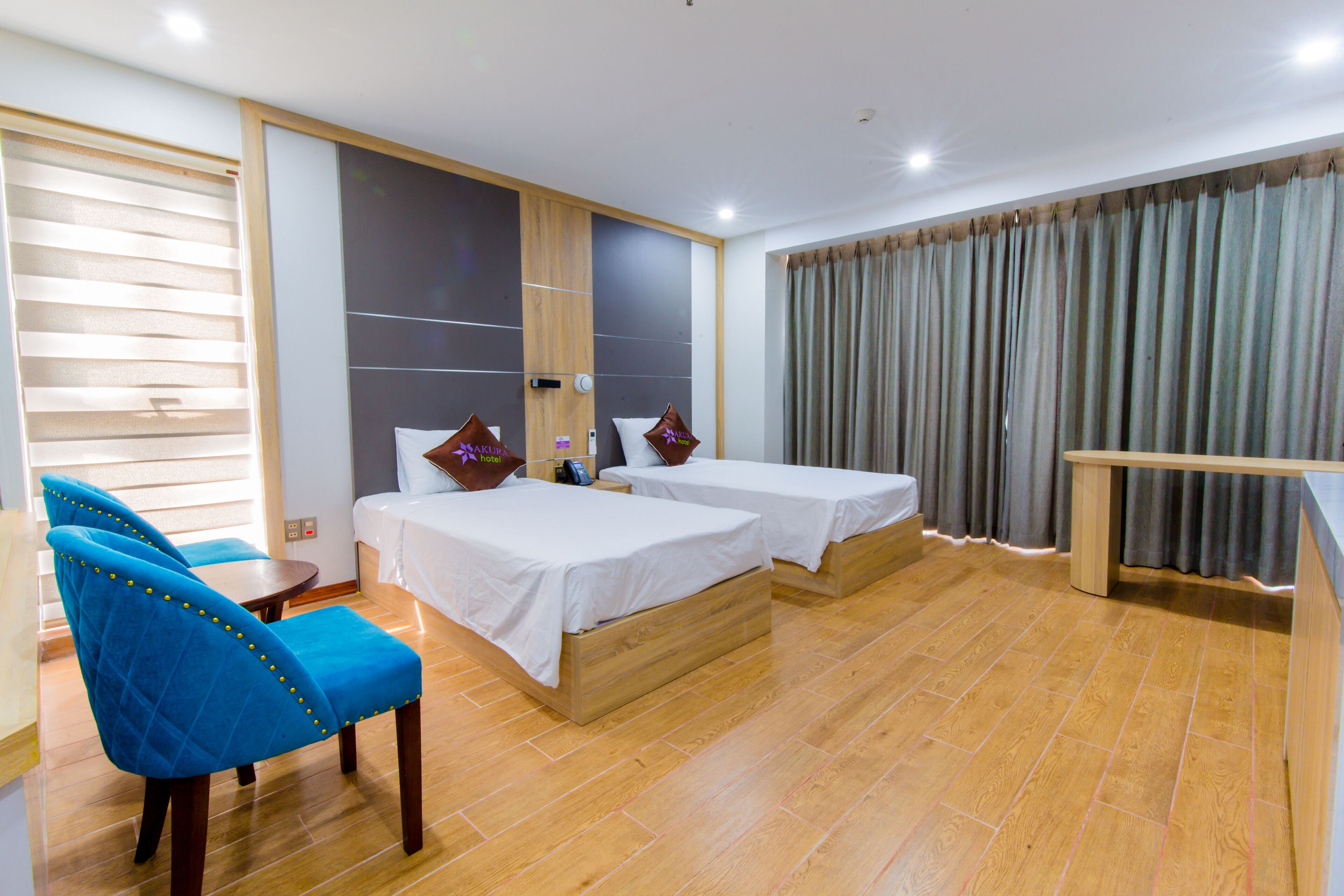 Habitación de hotel con dos camas, un escritorio, una silla y un ventanal con cortinas.