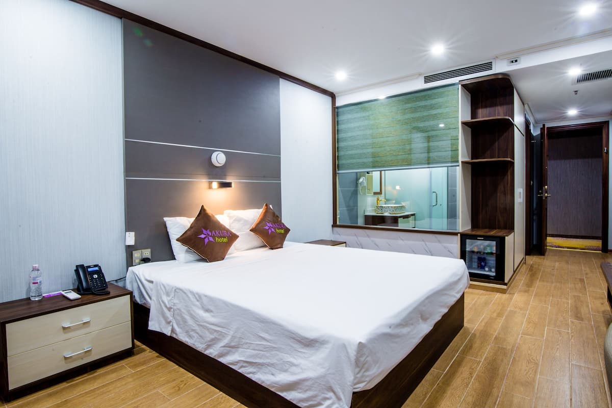 A hotel room with a large bed, bedside tables, a mirror, a wardrobe, and a minibar.