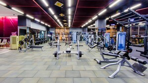 A gym with various exercise equipment, including weight machines and free weights, arranged in an open space with a tiled floor. - Sakura Hotel (Hoa Binh)