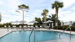 Uma piscina com espreguiçadeiras e guarda-sóis, cercada por palmeiras e uma vedação.