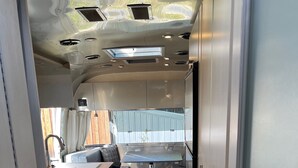 Un corredor estrecho y bien iluminado con un kitchenette a un lado, una zona de comedor con mesa y sillas, y un ventanal que ofrece vistas al exterior.