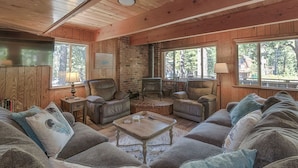 A cozy living room with wooden walls and ceiling, a brick fireplace, leather sofas, and a television. - Close drive to lake * Dog OK * Great Family Home (Carnelian Bay)