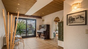 Um quarto espaçoso com um piano, vigas de madeira no teto e uma grande janela com vista para edifícios.