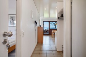 Un couloir avec un lit, une porte en bois, un porte-manteau et une vue sur un coin repas.