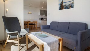 Un salon avec un canapé, un fauteuil, une table à manger et, au fond, un coin cuisine.
