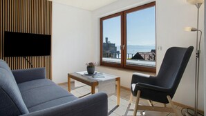 Un salon moderne comprenant un canapé, un fauteuil, une petite table avec une plante et une grande fenêtre donnant sur un paysage urbain.