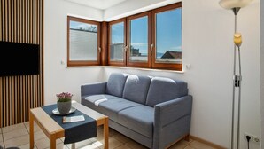 Una sala de estar moderna con un sofá, una mesa con una planta, un televisor montado en la pared y una lámpara de pie.