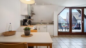 A modern kitchen with white cabinets, a dining table with chairs, a potted plant, and a large sliding glass door leading to an outdoor area. - Apartment DG4 in "Gästehaus Heinemann" Directly on Lake Constance (Langenargen)