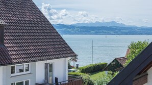 A residential building with a tiled roof, a balcony, and a view of a lake with mountains in the background. - Apartment DG4 in "Gästehaus Heinemann" Directly on Lake Constance (Langenargen)
