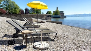 A beach with lounge chairs and a yellow umbrella, a stone wall, and a body of water in the background. - Apartment DG4 in "Gästehaus Heinemann" Directly on Lake Constance (Langenargen)